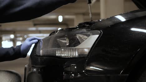 Disassembling-a-sedan-car-headlight-with-phillips-screwdriver-wearing-latex-gloves