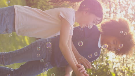 vertical video of smiling boy and girl outdoors having fun playing with bubbles in garden