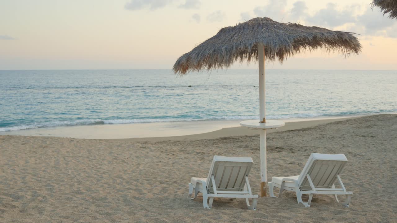 пляжный зонтик и пустые белые стулья с видом на красивое тропическое море на закате