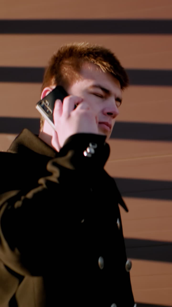 검은 코트 를 입은 사업가 가 전화 를 하는 동안 계단 을 내려가고, 서류 가방 을 들고 있으며, 건물 의 유리 창문 을 배경 으로 반사 하고 있다