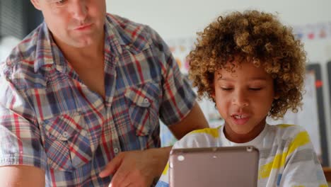 Front-view-of-Caucasian-male-teacher-teaching-schoolboy-on-digital-tablet-in-the-classroom-4k