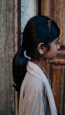 montage of a young south asian girl in simple clothing, standing near a weathered wooden door, her expressions shifting subtly across different frames