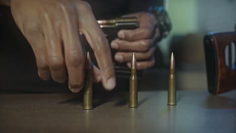 close up of man restocking a sniper rifle firearm magazine, putting bullet shells into holder one at time, war concept