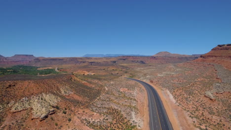 Aufsteigende-Drohnenaufnahme-Einer-Langen-Straße,-Die-Durch-Den-Berg-Zion-Führt,-Mit-Einer-Bergkette-Im-Hintergrund-Im-Süden-Von-Utah