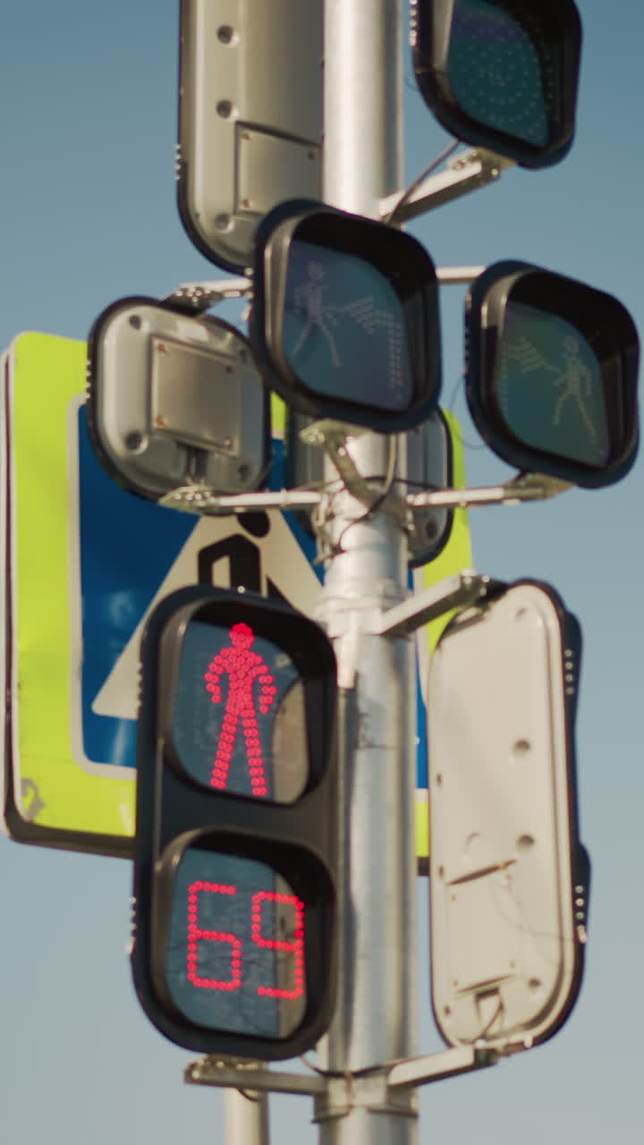 red pedestrian signal countdown on pole, urban intersection closeup showing LED timer decreasing from to , red walking silhouette illuminated, signage and metal housing visible against clear
