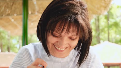 Attractive-young-female-with-short-brunette-hair-and-green-eyes-plays-with-a-straw,-looks-at-the-camera-and-smiles-genuinely