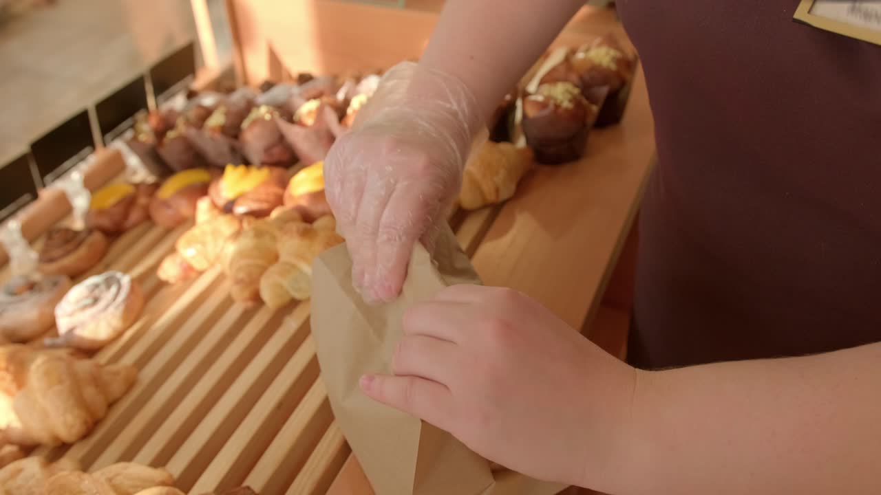 Woman Packaging Croissant in Brown Paper Bag at Bakery