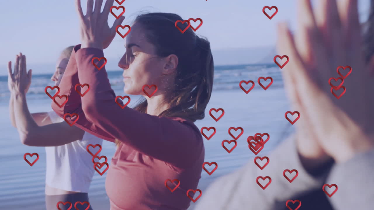 Women practicing yoga on beach with heart animations overlaying scene