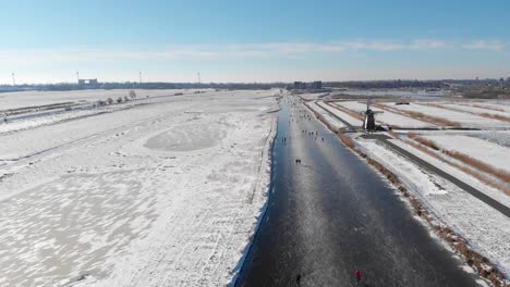 People-ice-skating-on-frozen-Dutch-canal-in-windmill-polder-land,-winter-scene