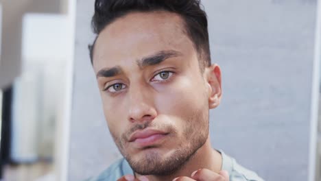 Focused-biracial-man-looking-in-bathroom-mirror,-examining-his-face-and-skin,-slow-motion