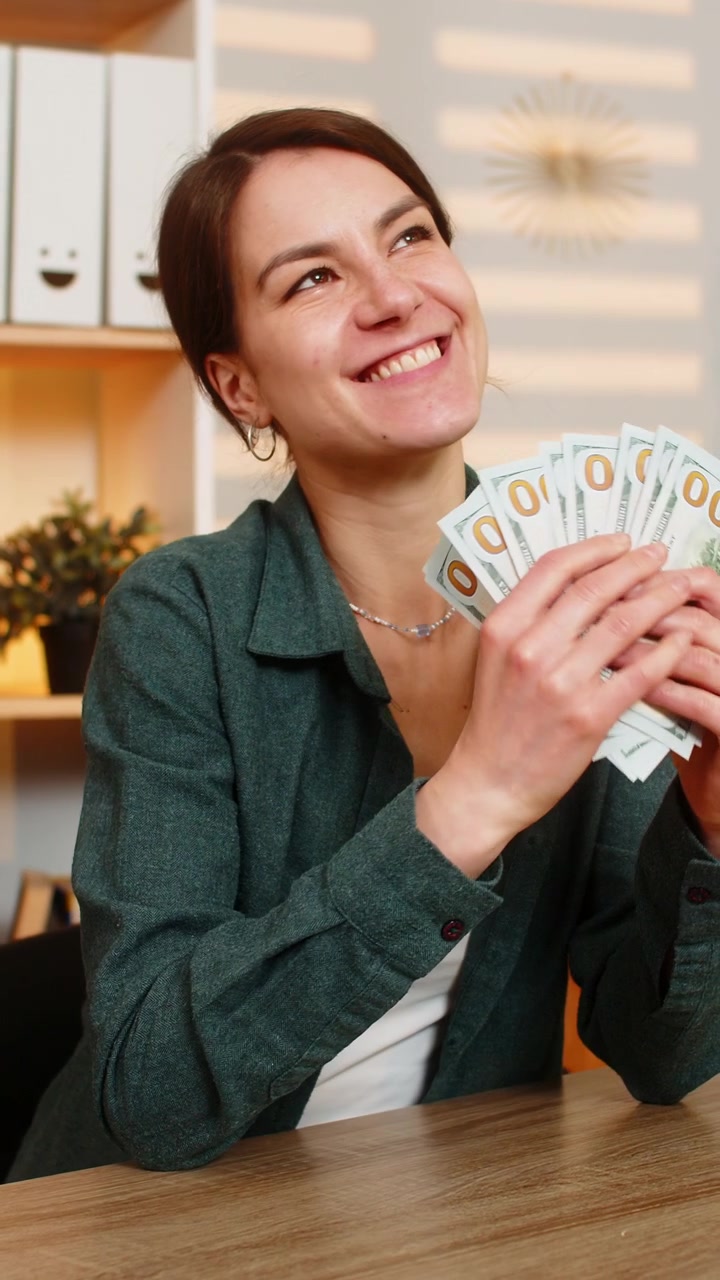 Mujer joven en la mesa de casa contando dinero en efectivo, planificando gastos del presupuesto y sintiéndose feliz en la sala de estar