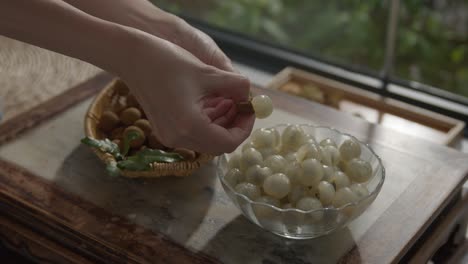 peeling longan fruit in a bowl, sweet snack on a table