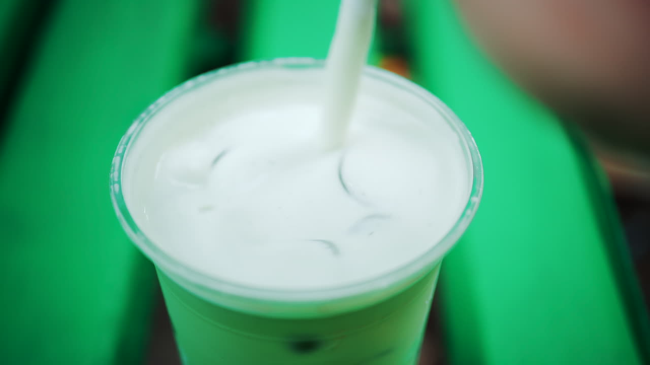 Close up of an iced matcha being stirred in a glass on a green park bench