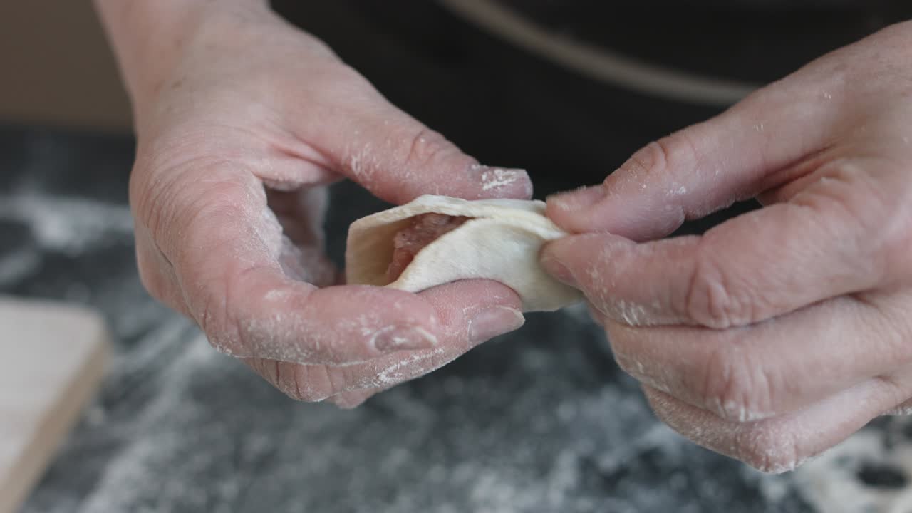 Two hands making meat dumplings.