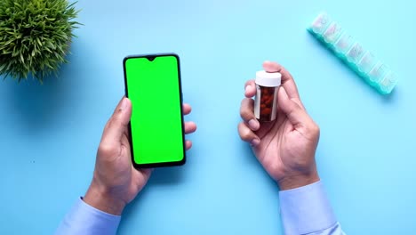 hombre joven con la mano sosteniendo un teléfono inteligente y un recipiente de pastillas médicas