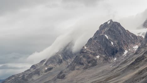 las nubes y la niebla parecen derramarse sobre los picos montañosos irregulares en groenlandia