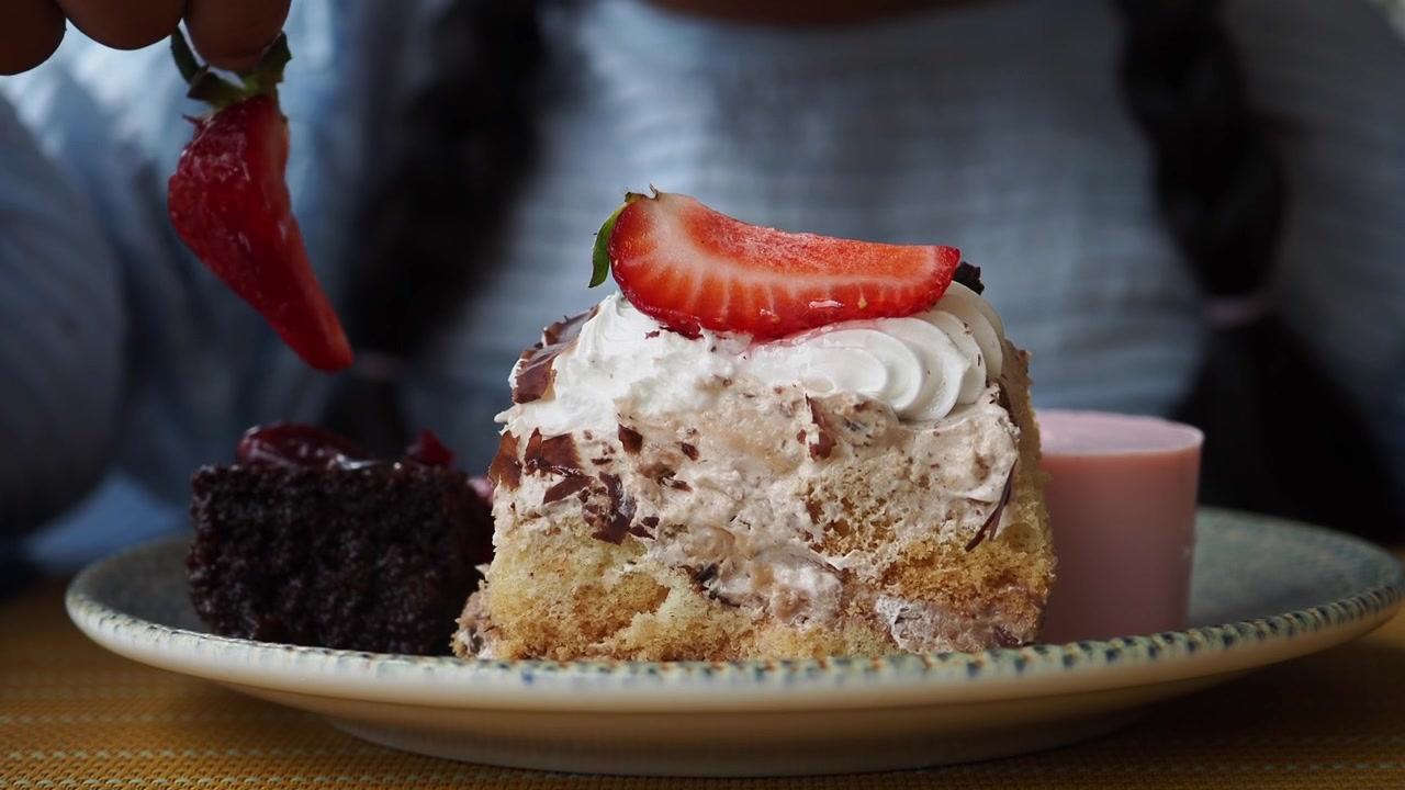 Primo piano di mano che prende una fragola da un piatto di dolci