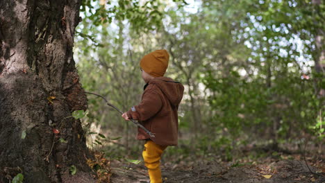 smiling baby boy holding a long stick. toddler plays happily in the nature. blurred backdrop.