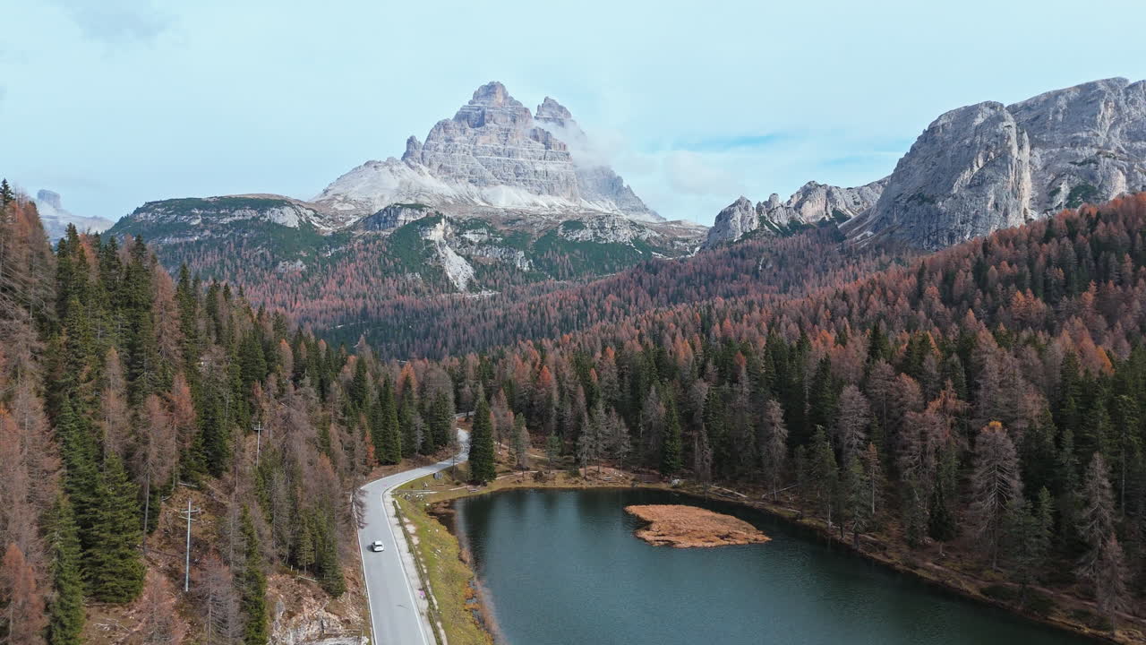 Mountain lake with scenic autumn forest and Tre Cime di Lavaredo peaks under a clear sky