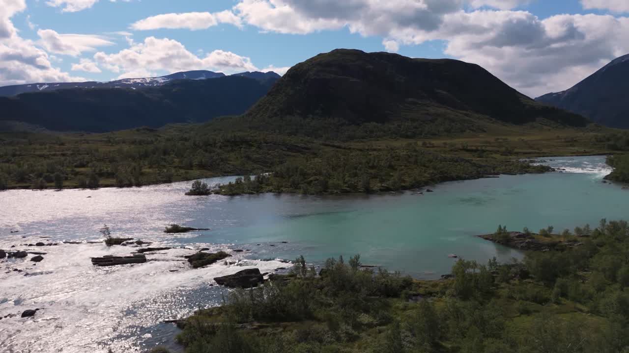 vista aérea que muestra un río sereno que fluye a través de un pintoresco paisaje montañoso con cielos azules claros y nubes dispersas