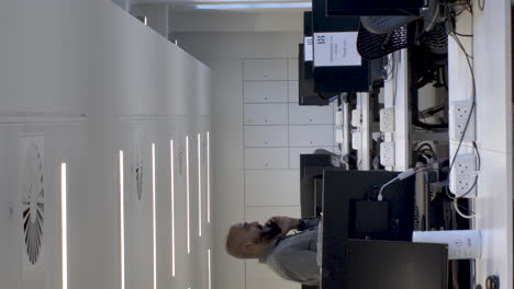 bald ethnic minority male talking on phone walking in between empty desks. vertical video, locked off
