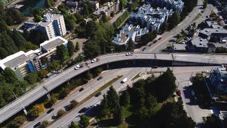 Luftaufnahme-über-Der-Überführung-Leichter-Verkehr-Auf-Allen-Fahrspuren-Vogelperspektive-Niedrige-Wohnungen-Hohe-Bäume-Ein-Schwarzer-Geländewagen-Ein-Gelber-Taxivan,-Der-Mit-Bauarbeitern-Und-Auf-Dem-Seitenstreifen-2-5-Geparkten-Fahrzeugen-überquert-Wird