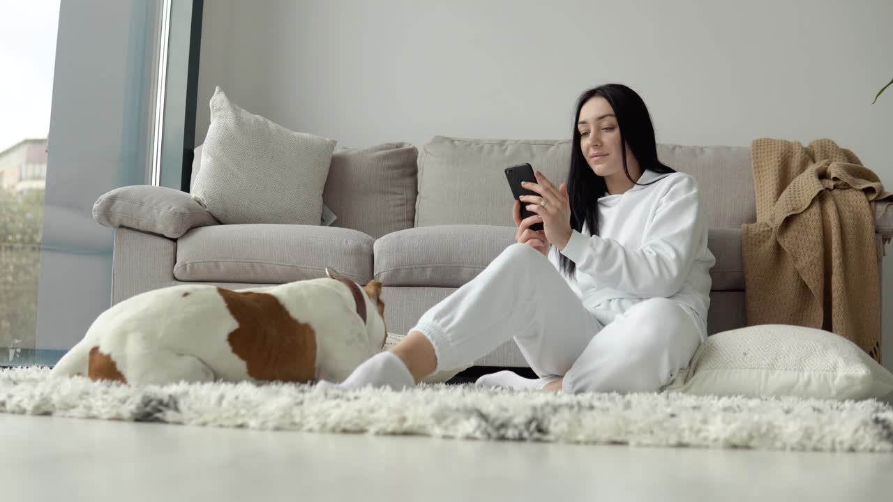 Young woman relaxing with her dog and use phone in a beautiful modern apartment
