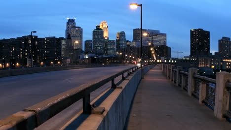 Schwenken-Sie-Nach-Links-über-Die-Lichtstreifen-Des-Beschleunigten-Verkehrs,-Um-Den-Vordergrund-Zu-Betonen,-Während-Die-Skyline-Von-Minneapolis-Im-Verblassenden-Sonnenlicht-Dunkler-Wird