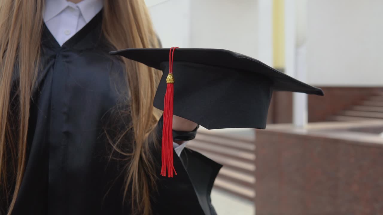sombrero de maestro con una borla roja en la mano de un graduado universitario. vista de cerca con un fondo al aire libre