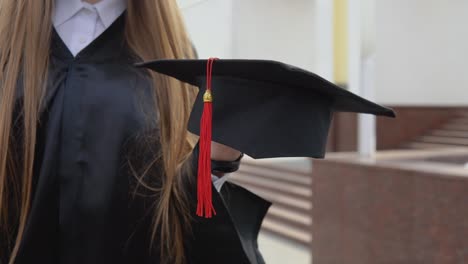 master's hat with a red tassel on the hand of a university graduate. close up view with a outdoor background