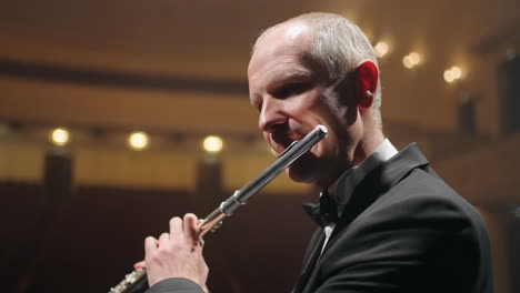 man is playing flute on scene of opera house or philharmonic hall closeup portrait of talented flutist