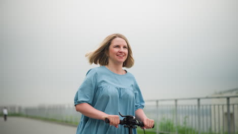 a smiling woman rides a scooter down a pathway, enjoying a leisurely outdoor moment