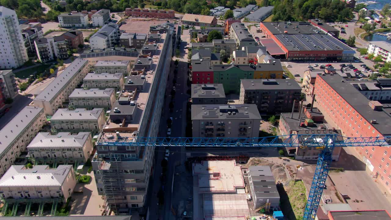 Vista aérea superior de uma construção em andamento, com um grande guindaste entre fileiras de apartamentos modernos e prédios coloridos em Gustavsberg