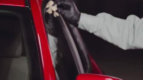 ingeniero con guantes negros y usando un paño de microfibra verde para limpiar el espejo de la ventana lateral del coche rojo