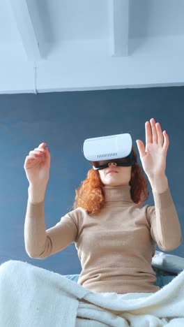 young woman wearing virtual reality headset is engaged in immersive experience while sitting on a cozy bed with soft blanket, showcasing modern technology and interaction