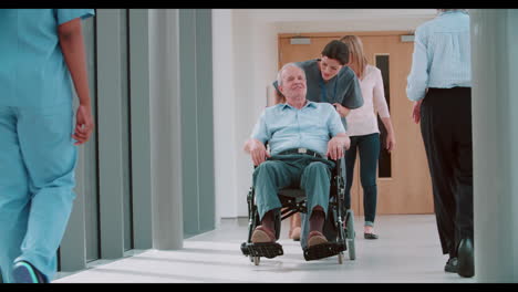 Nurse-Pushing-Senior-Patient-In-Wheelchair-Along-Corridor