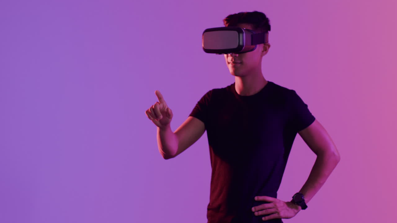 Asian man using vr headset, touching virtual screen on purple background, copy space, slow motion
