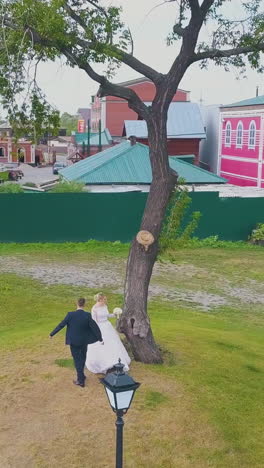 happy young couple dances on lawn at beautiful christian church fence on warm autumn day aerial view
