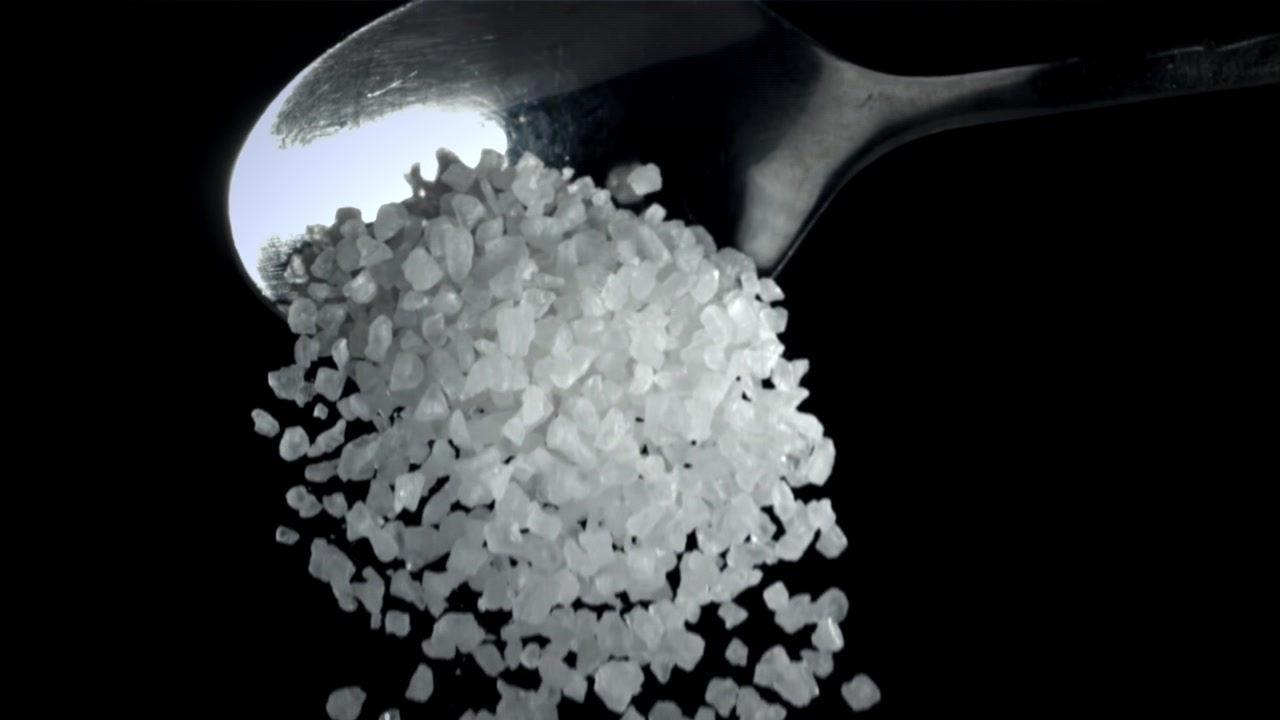 Slowmotion af groft salt, der drysser fra en ske