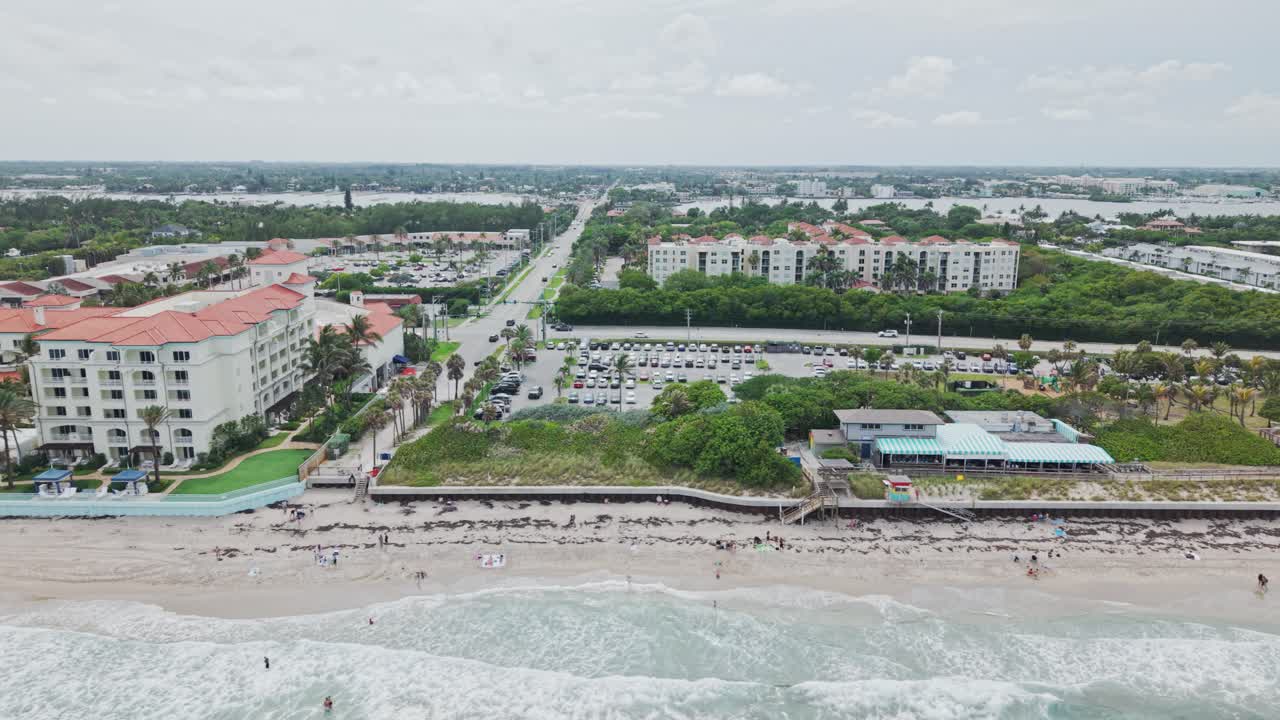 Aerial: beach and hotels next to Atlantic Ocean with cloudy weather during the day in West Palm Beach, Florida, USA, pan drone shot