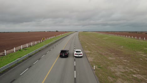 aéreo - dos autos en carretera vacía, adelante, día nublado, reynosa, tamaulipas, méjico