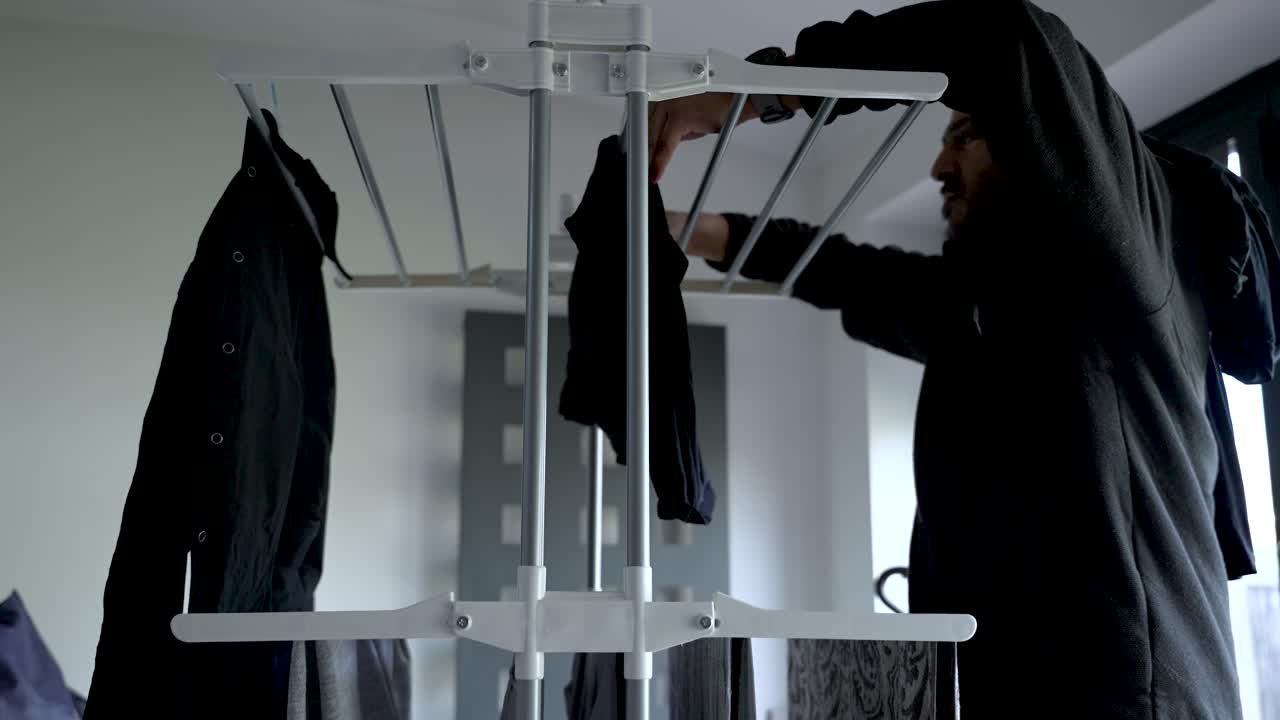 Person Hanging out clothes onto drying rack indoors