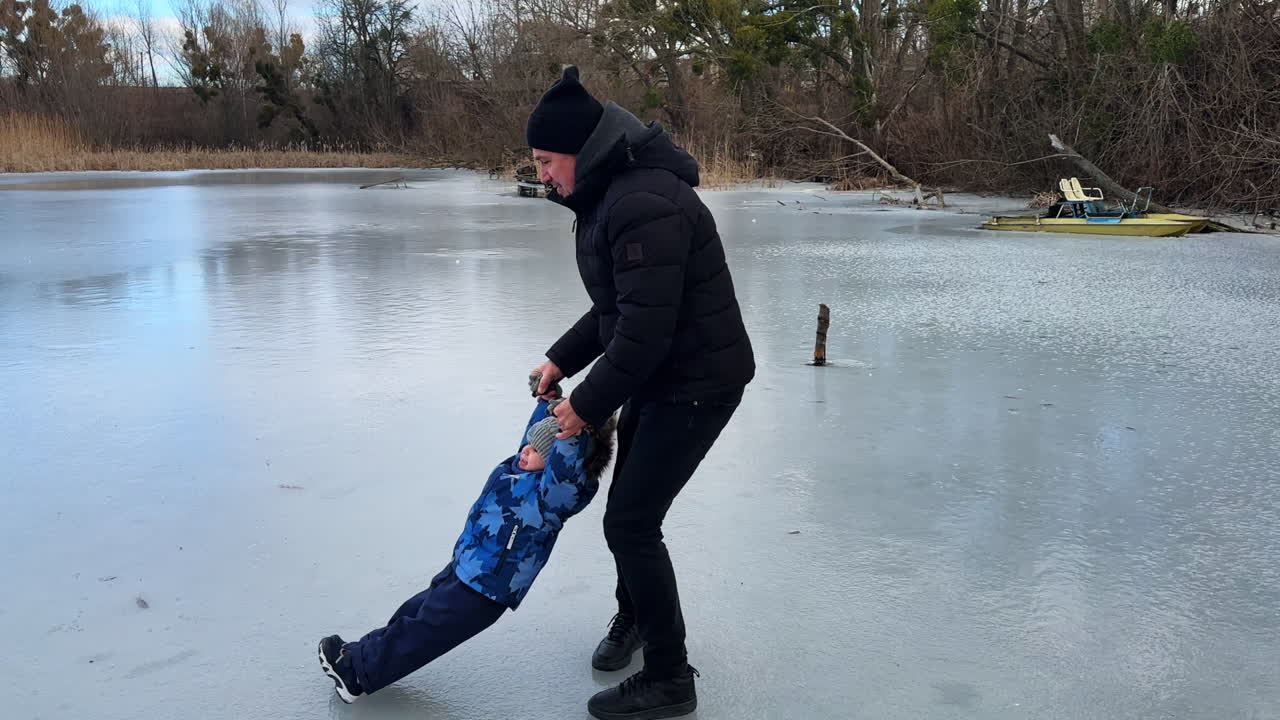 Caucasian man turning around on the ice holding his son by the hands. Dad with his baby in the nature in winter.