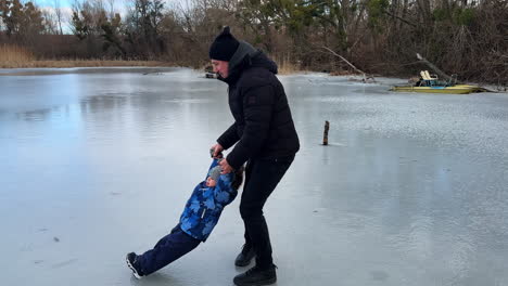 caucasian man turning around on the ice holding his son by the hands. dad with his baby in the nature in winter.