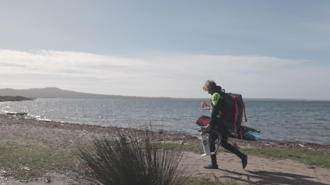 Kitesurfer con la sua attrezzatura che cammina lungo la spiaggia in una giornata di sole - campo lungo