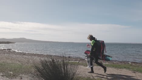 Kitesurfer-With-His-Equipment-Walking-Along-The-Beach-On-A-Sunny-Day---wide-shot