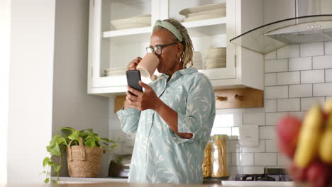 A-senior-African-American-woman-is-drinking-coffee-and-looking-at-smartphone