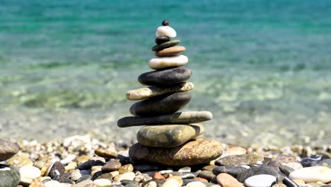 zen stacked rocks on a beach with crystal clear water in the background in sardinia, italy