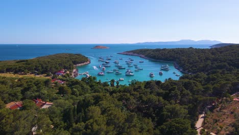 yates en la bahía cerca de la ciudad costera de croacia con el telón de fondo de cielos azules y agua azul transparente, árboles verdes y casas con techos rojos