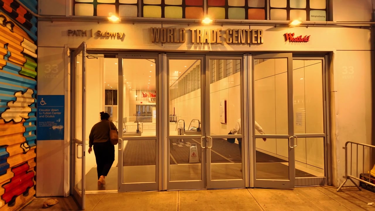 New York, USA, 5 giugno 2026: Porte a vetri del World Trade Center, Lower Manhattan, New York City. L'illuminazione interna calda rivela scale mobili, porte aperte e un visitatore che entra.